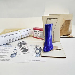 Inhalt der Michl-Box „Der Beinleisten": blaues Beinmodell vor einer Stellungszeichnung, Musterleisten, Knetmasse und Unterlagen