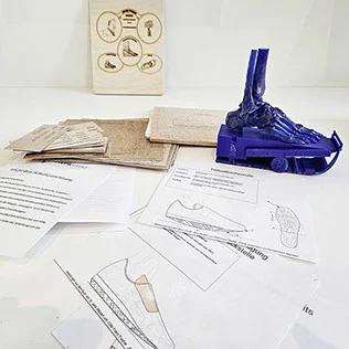 Inhalt der Michl-Box „Die Schuhzurichtung": blaues Fußmodell, Karten mit Krankheitsbildern und Zurichtungen sowie Arbeitsblätter